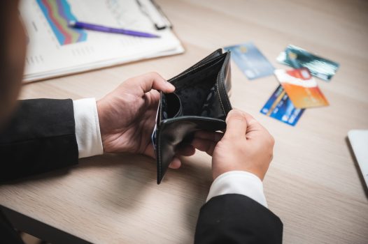 High angle closeup view of hands of a businessman in formal clothing looking at an empty wallet with cards and financial report on table